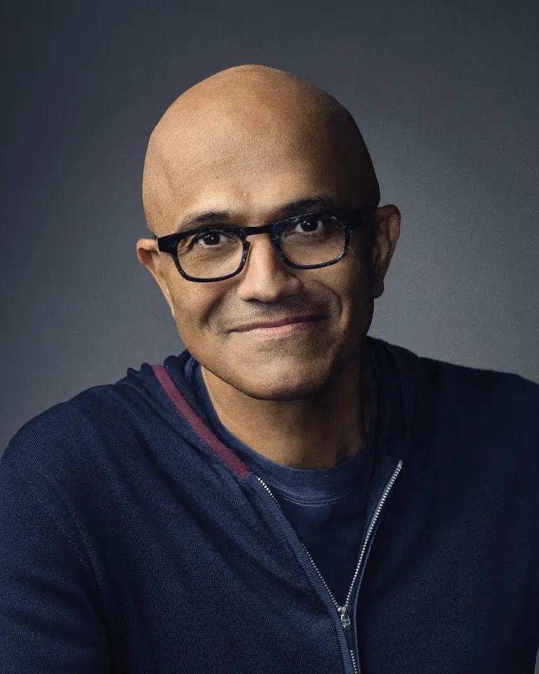 Portrait de Satya Nadella, PDG de Microsoft, souriant, en sweat bleu marine.